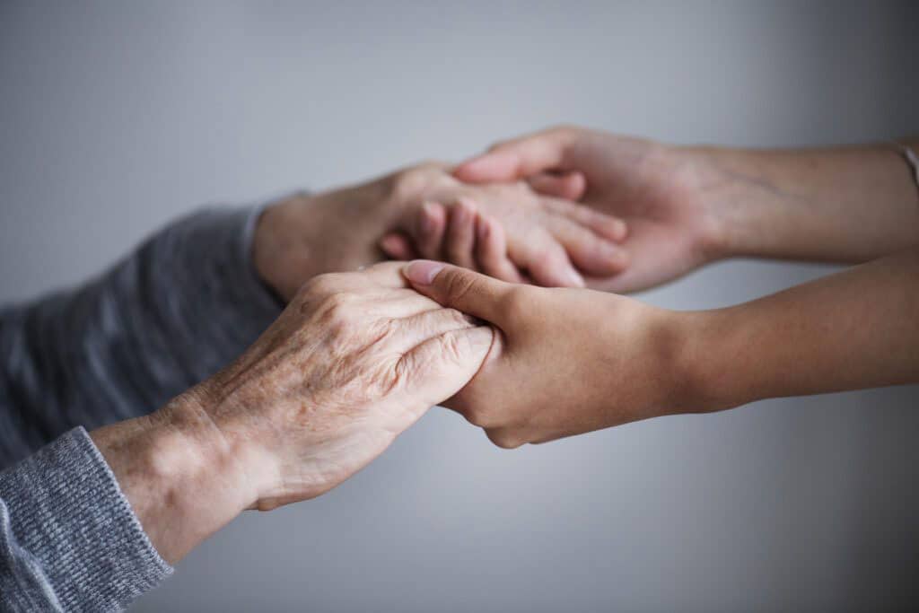 Krankenschwester hält die Hände eines älteren Mannes, um Trost und Sicherheit zu spenden.