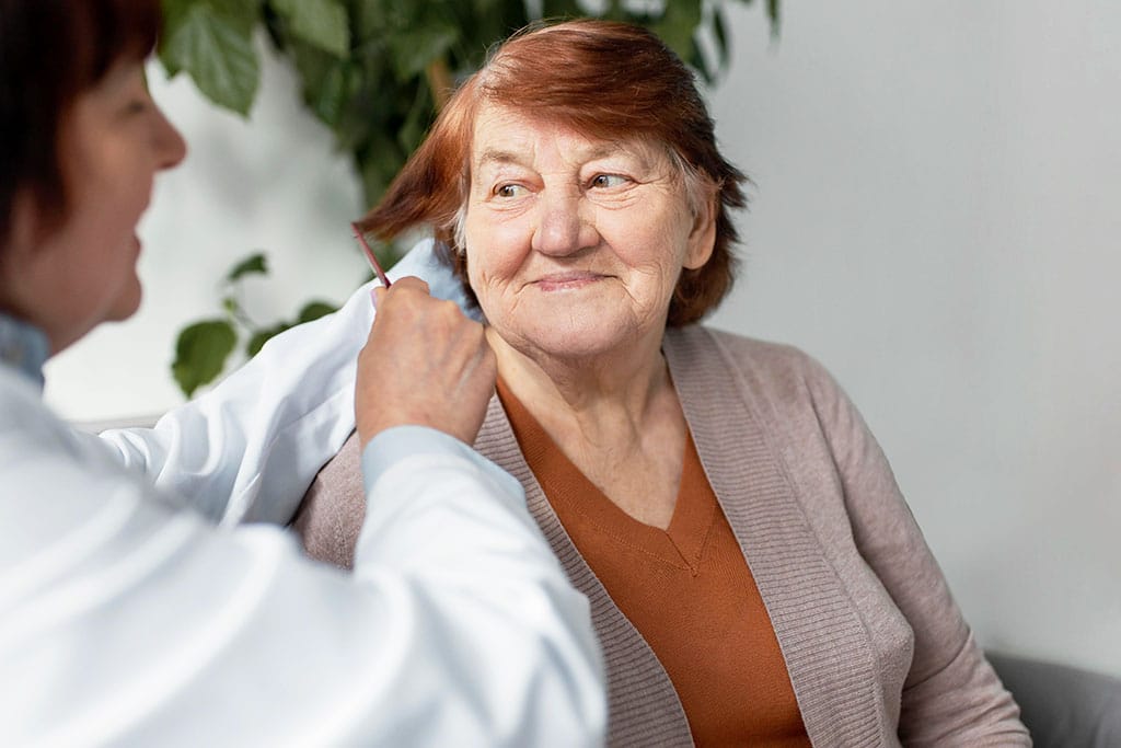 Krankenschwester richtet das Haar der älteren Frau, während diese sie lächelnd anschaut.