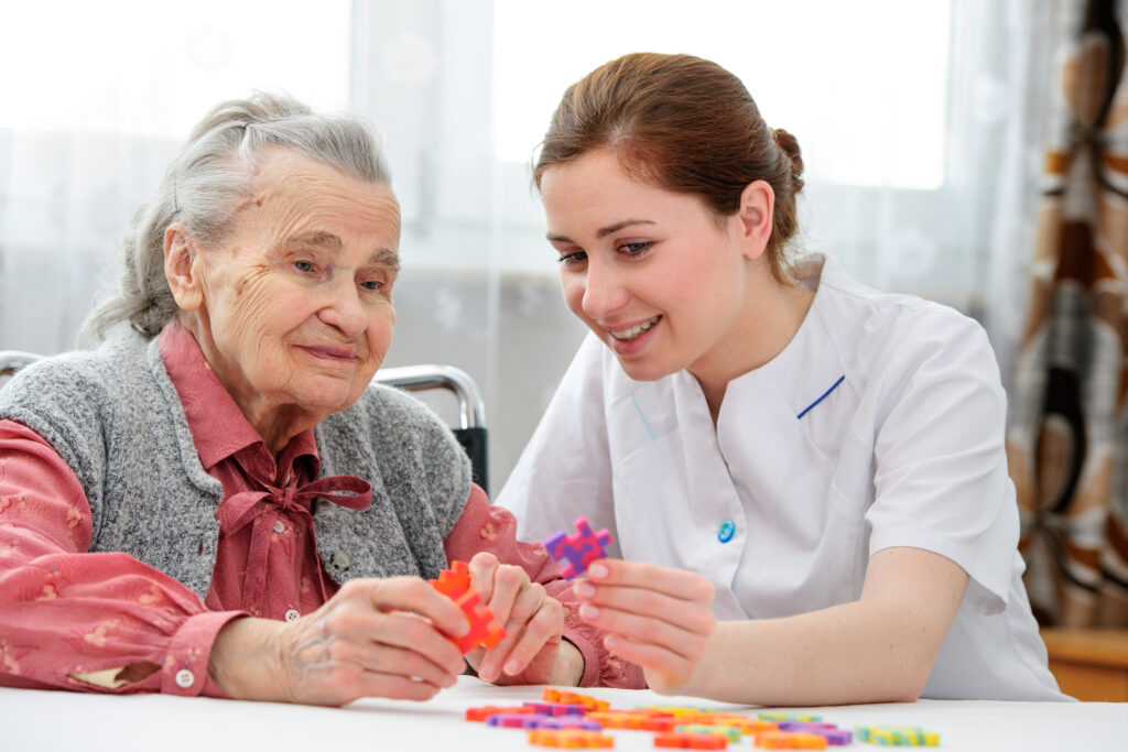 Pflegekraft spielt mit Seniorin im Pflegeheim ein Puzzle.